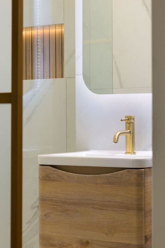 Modern bathroom with wooden vanity, white sink, brass tap and mirror