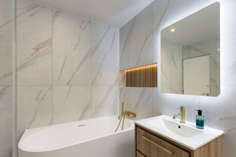 Modern bathroom with marble walls, freestanding bathtub, illuminated mirror and wooden vanity
