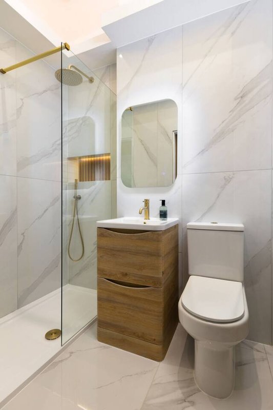 Modern bathroom with marble tiles, wooden vanity, mirror, toilet and glass shower enclosure