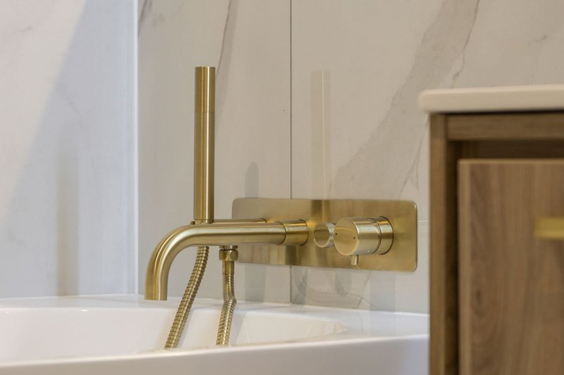 Modern bathroom with brass wall-mounted faucet and white bathtub edge
