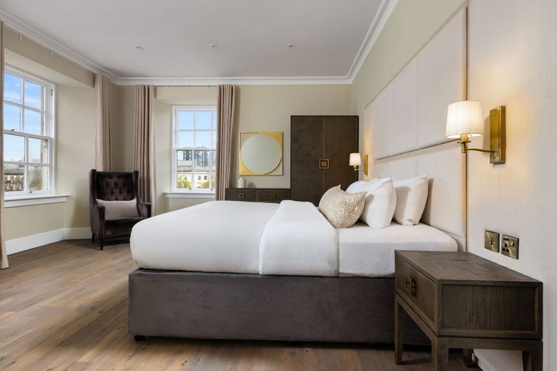 Spacious modern bedroom with king bed, armchair, windows and wooden flooring