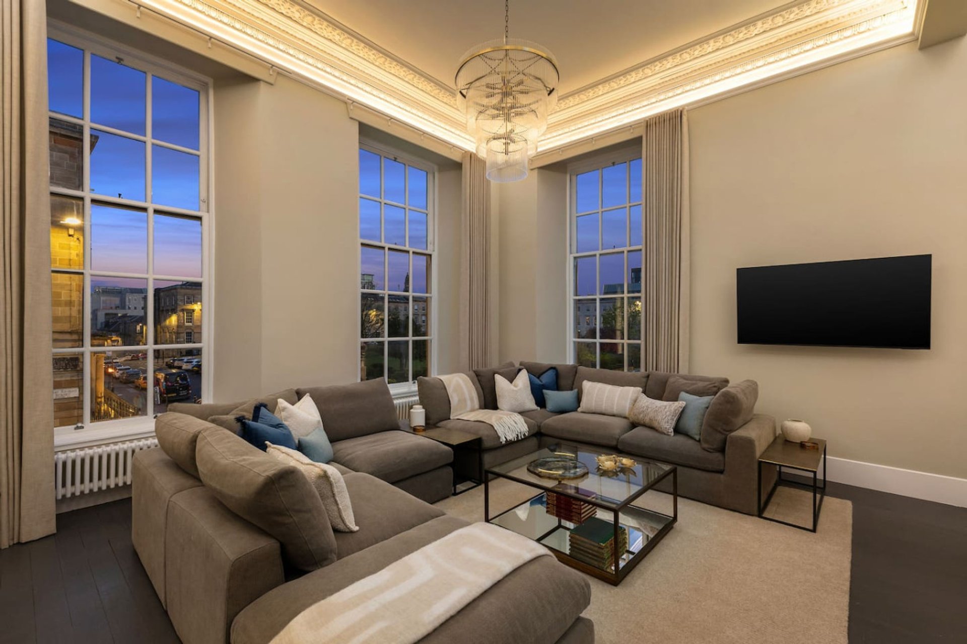 Spacious living room with wraparound sofa, large windows, mounted TV and elegant ceiling fixture