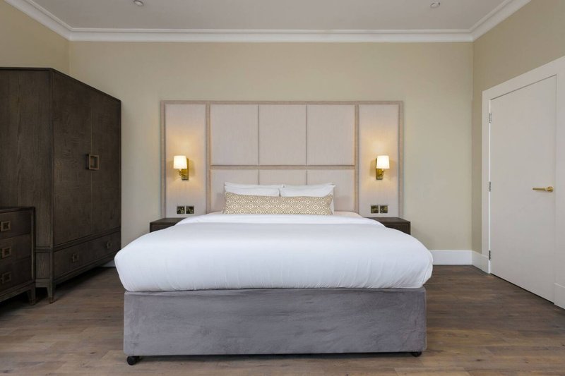 Modern bedroom with large bed, upholstered headboard, wall sconces, and wooden flooring