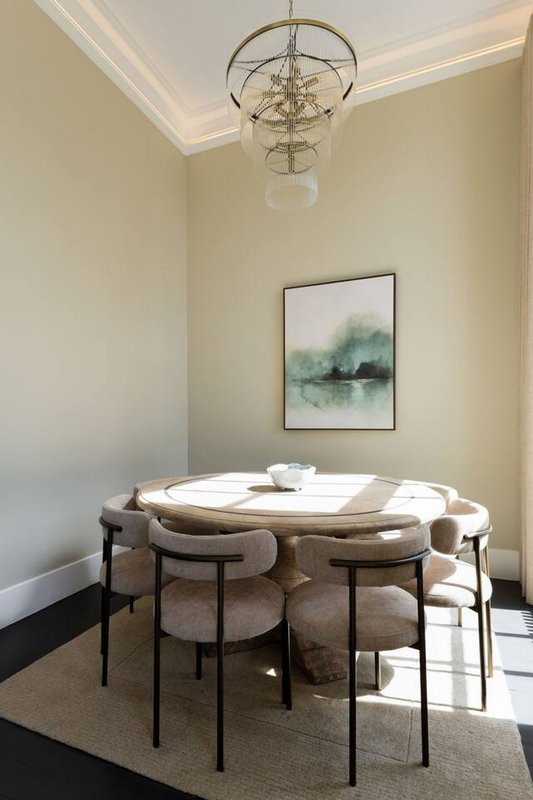 Dining room with round table, upholstered chairs, pendant light fixture and framed landscape artwork