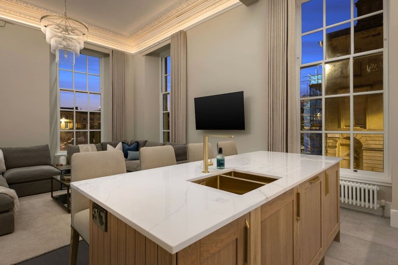 Modern open-plan kitchen and living room with white marble island, wooden cabinetry, and city views