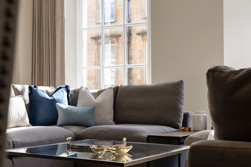 Modern living room with grey sofa, blue and grey cushions, glass coffee table and large window