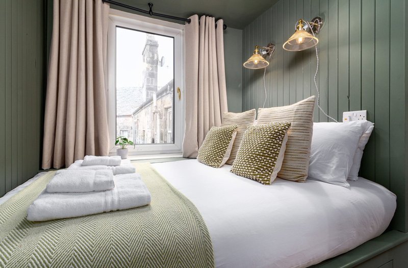 Modern bedroom with double bed, green panelled walls, pendant lights and city view from window