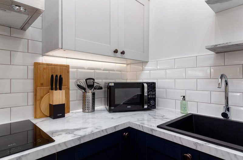 Modern kitchen with white cabinetry, marble countertop, black microwave and sink