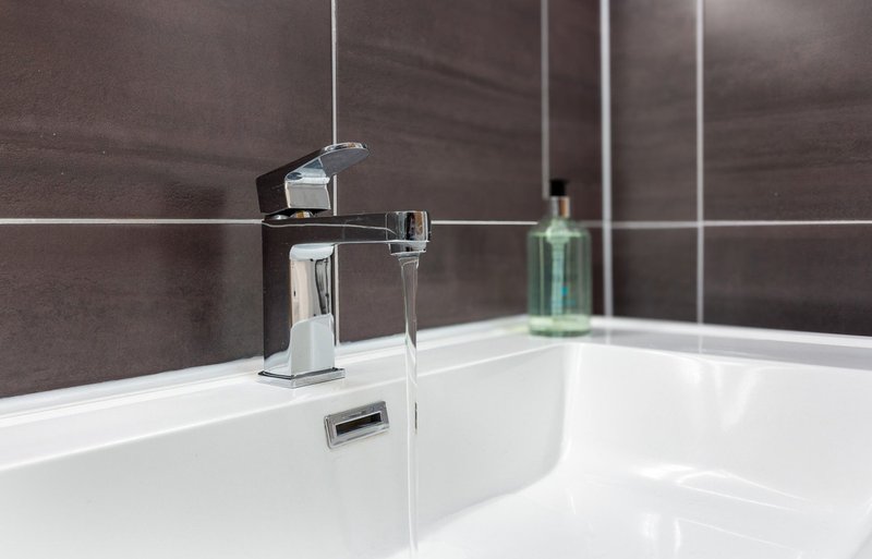 Modern bathroom sink with chrome faucet, white basin, and brown tile wall