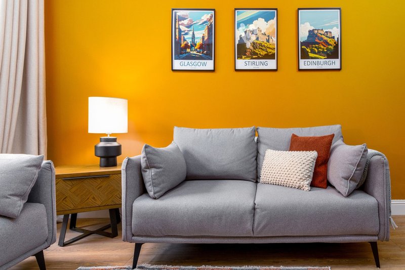 Modern living room with gray sofa, yellow wall, framed travel posters and table lamp