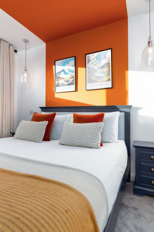 Modern bedroom with orange accent wall, double bed, decorative pillows and framed artwork