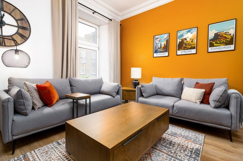 Modern living room with gray sofas, wooden coffee table, orange accent wall and framed artwork