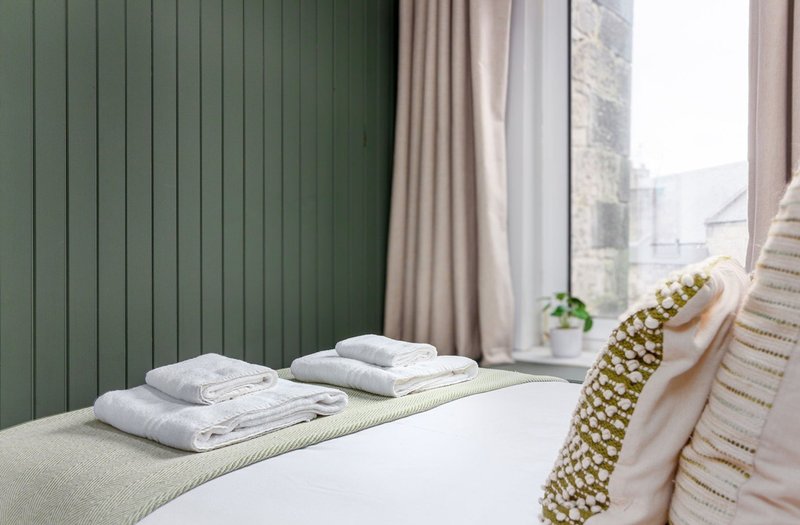Bedroom with folded white towels on bed, green paneled wall, and window with curtains