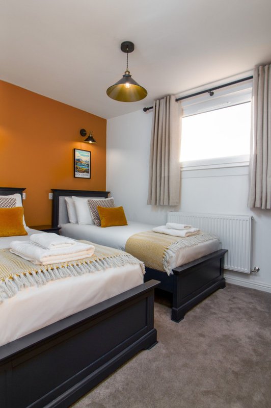 Twin bedroom with two single beds, orange accent wall, pendant lamp and window with curtains