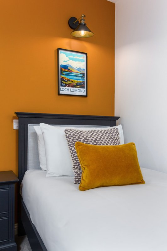 Bedroom with bed, yellow cushion, white pillows, orange wall and framed art