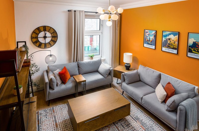 Living room with two gray sofas, wooden coffee table, orange accent walls, and decorative framed prints
