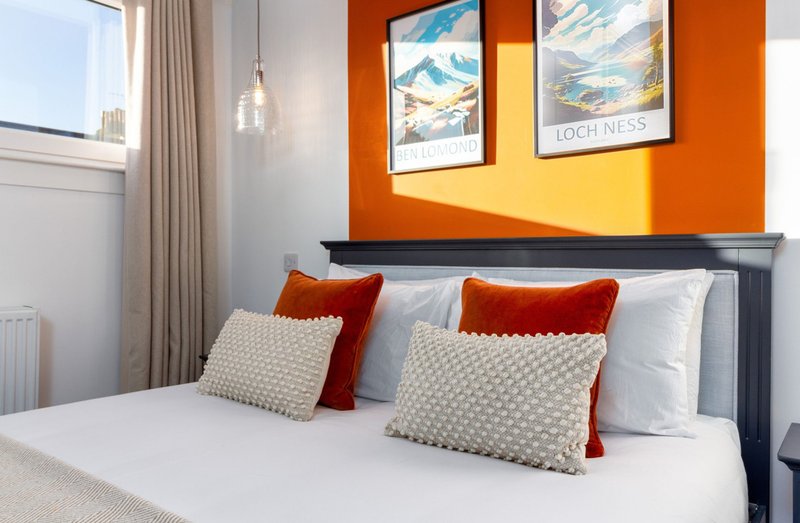 Modern bedroom with double bed, red and cream cushions, orange accent wall and framed prints