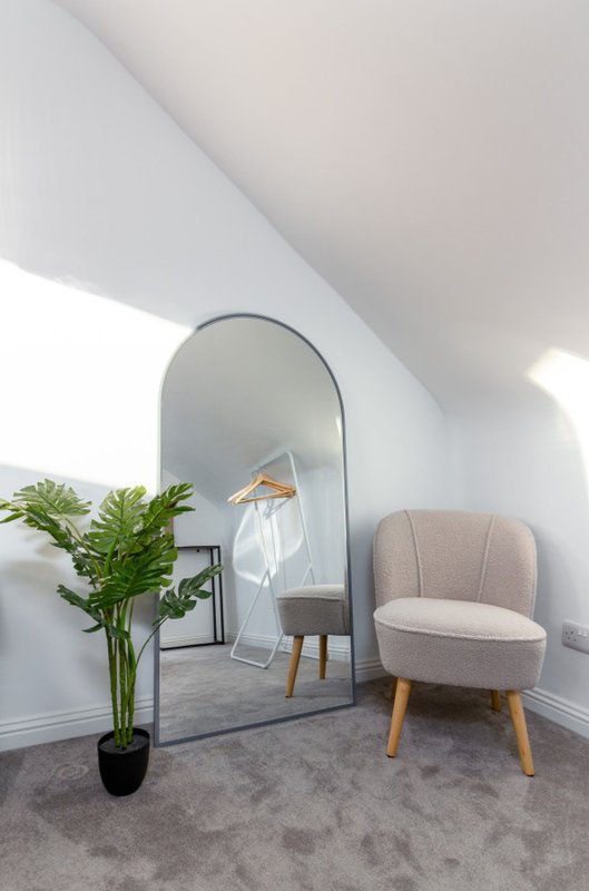 Bright modern room with arched mirror, beige armchair, potted plant and wooden accent table