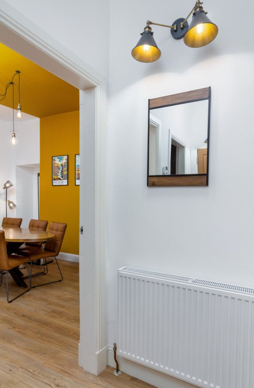 Modern hallway with pendant lights, framed mirror, radiator and view into yellow-painted study room