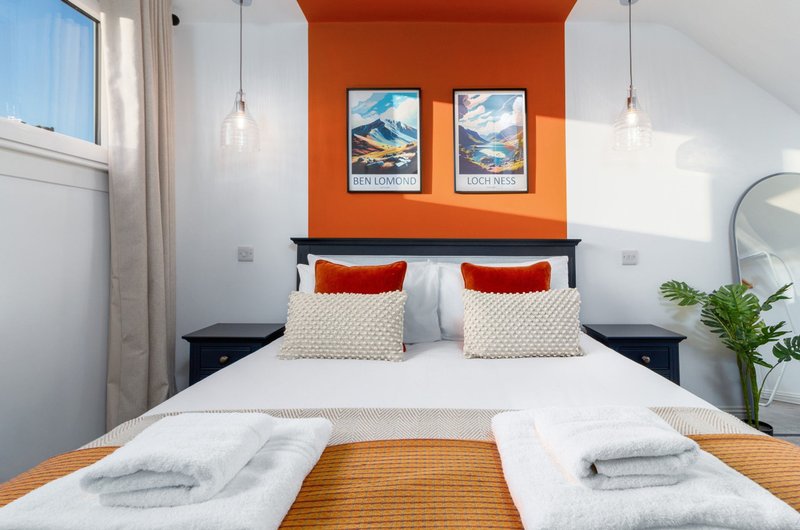 Bright modern bedroom with orange accent wall, double bed, pendant lights and mountain prints