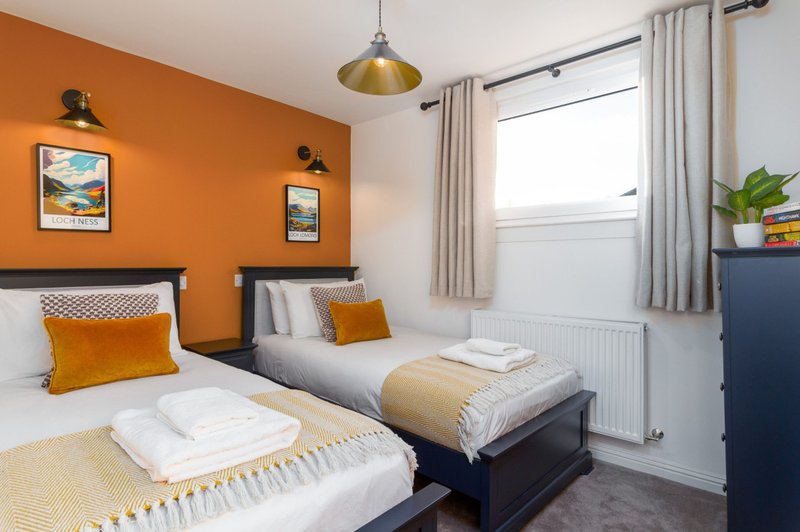 Bright twin bedroom with orange accent wall, single beds, pendant light, and large window
