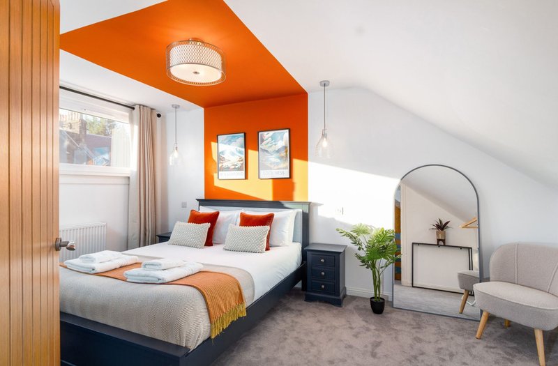 Bright attic bedroom with orange ceiling, double bed, window, and modern furnishings