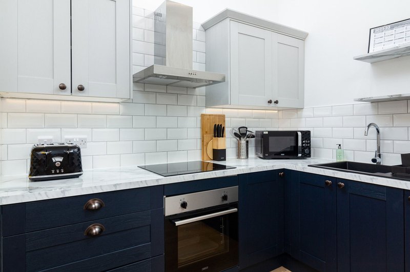 Modern kitchen with white and navy cabinetry, subway tile backsplash, stainless steel appliances and black countertop