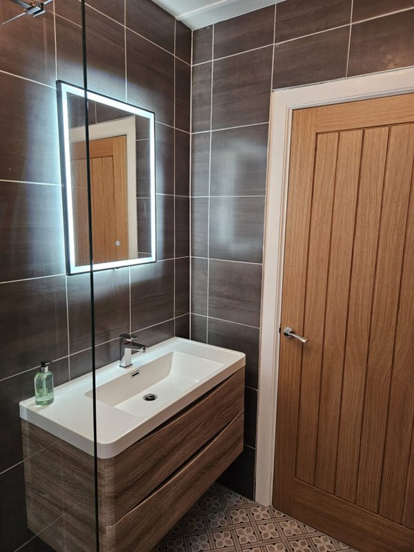 Modern bathroom with illuminated mirror, white sink, wooden vanity, and glass shower enclosure