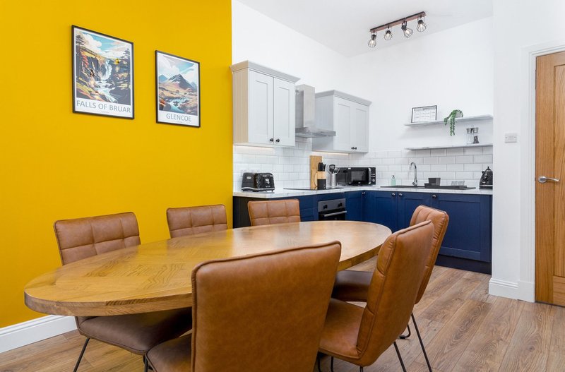 Open-plan kitchen and dining area with yellow accent wall, wooden oval table, and blue cabinetry