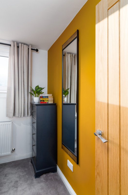 Modern bedroom corner with yellow accent wall, mirror, potted plants, and wooden door