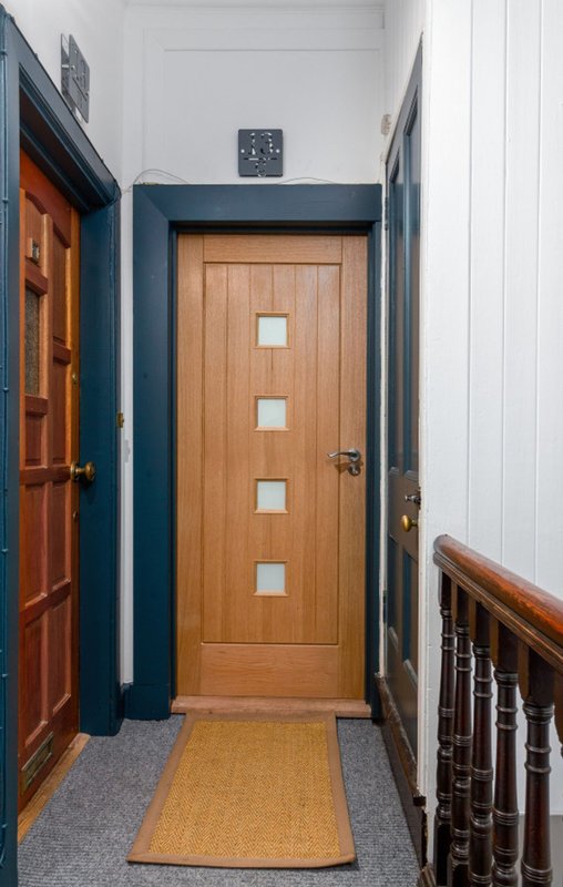 Hallway with wooden door, blue-painted frame, and stair railing on right side