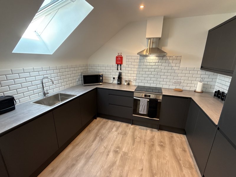 Modern kitchen with black cabinetry, white subway tiles, skylight, and wooden flooring