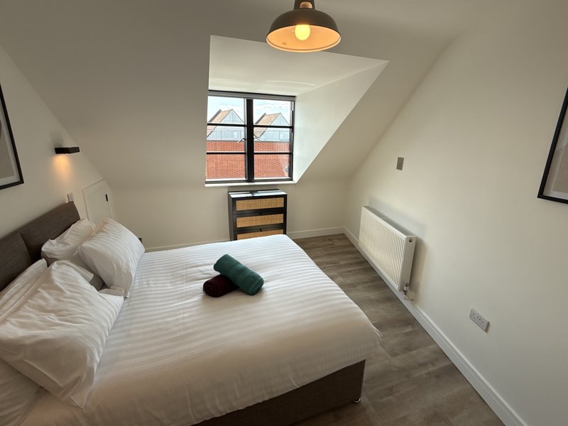 Modern bedroom with double bed, pendant light, wooden dresser and sloped ceiling