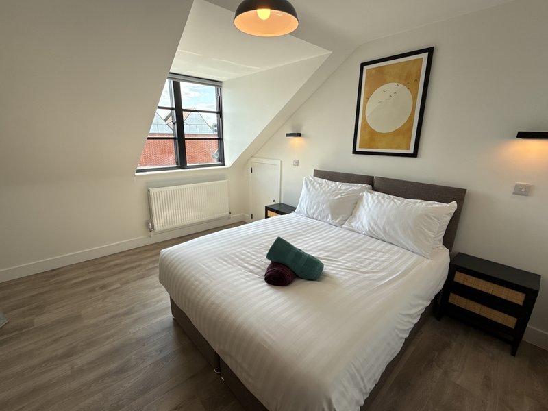 Modern bedroom with double bed, dark wood frame, white bedding, wooden floor and pendant light