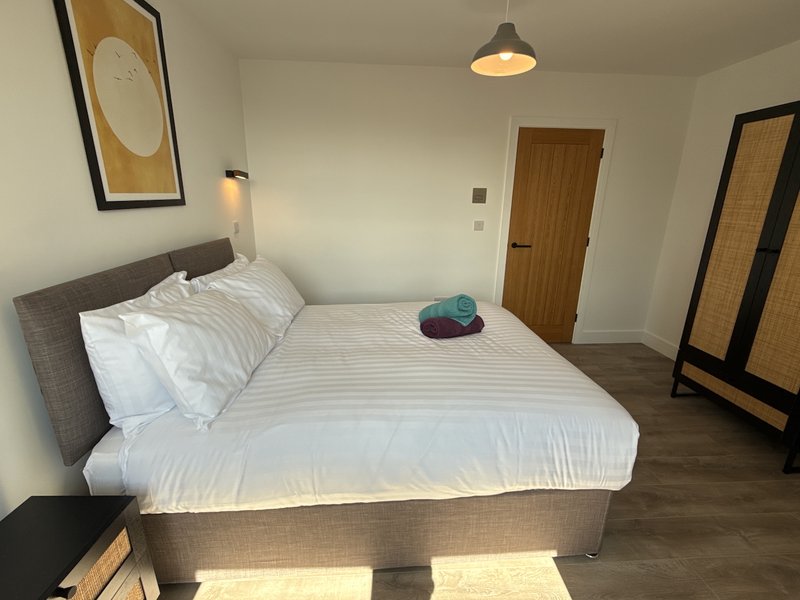 Bedroom with gray upholstered bed, white bedding, wooden doors, pendant light, and framed wall art