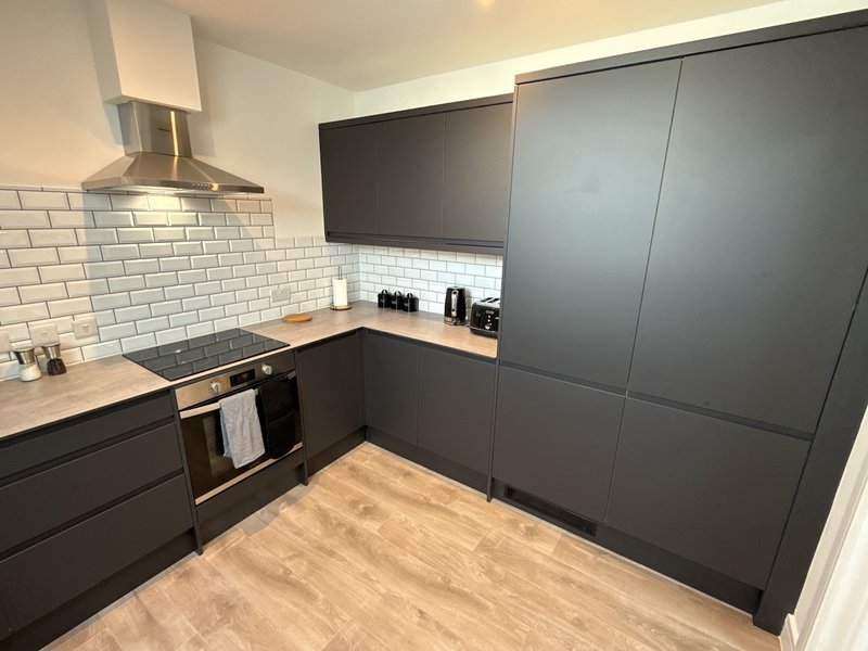 Modern kitchen with dark cabinetry, white subway tile backsplash, wood countertop and wooden flooring