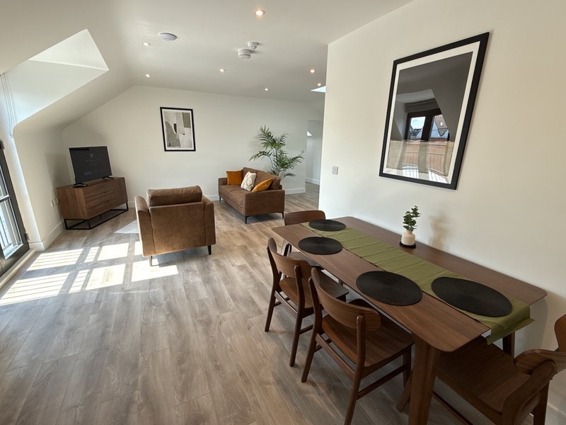 Spacious open-plan living and dining area with wooden furniture, armchairs, and natural light from skylights