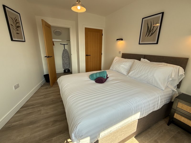 Bedroom with double bed, white bedding, wooden doors, framed wall art and pendant light