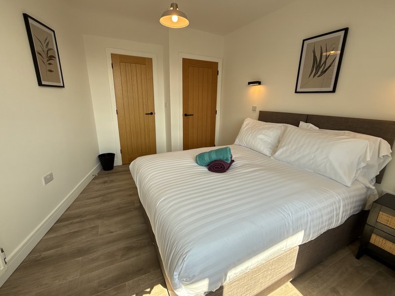Bedroom with double bed, white bedding, wooden doors, framed wall art and pendant lighting