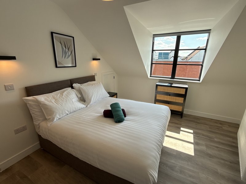 Modern bedroom with double bed, white bedding, wooden nightstands, and skylight window