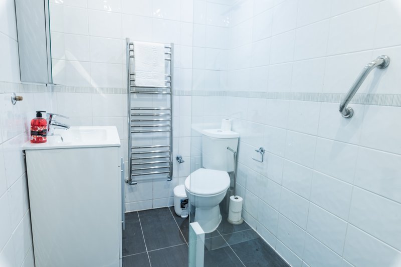 Modern bathroom with white tiles, toilet, heated towel rail, sink and shower enclosure