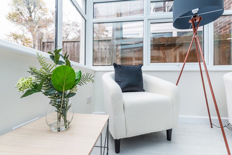 Bright modern living room with white armchair, wooden table, potted plant and tripod floor lamp