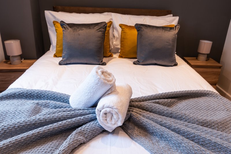 Modern bedroom with neatly made bed, decorative pillows, rolled towels and bedside lamps
