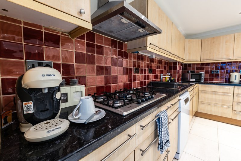 Kitchen with red tile backsplash, gas hob, cream cabinets and black countertop