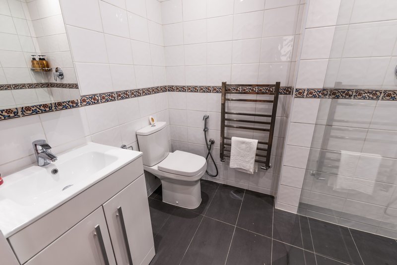 Clean bathroom with white sink vanity, toilet, heated towel rack and dark tile flooring