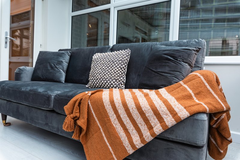 Dark grey sofa with patterned cushions and orange striped throw blanket, near windows