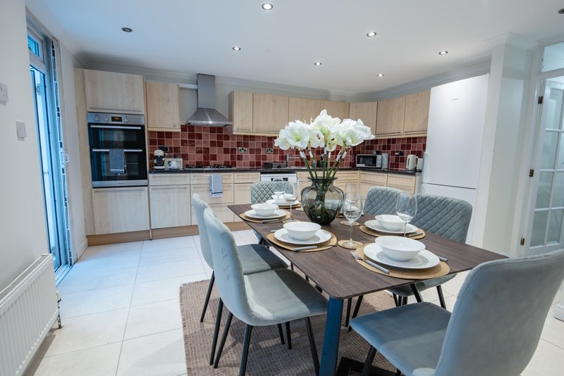 Modern open-plan kitchen and dining area with wooden cabinets, red tile backsplash, and dining table set for four