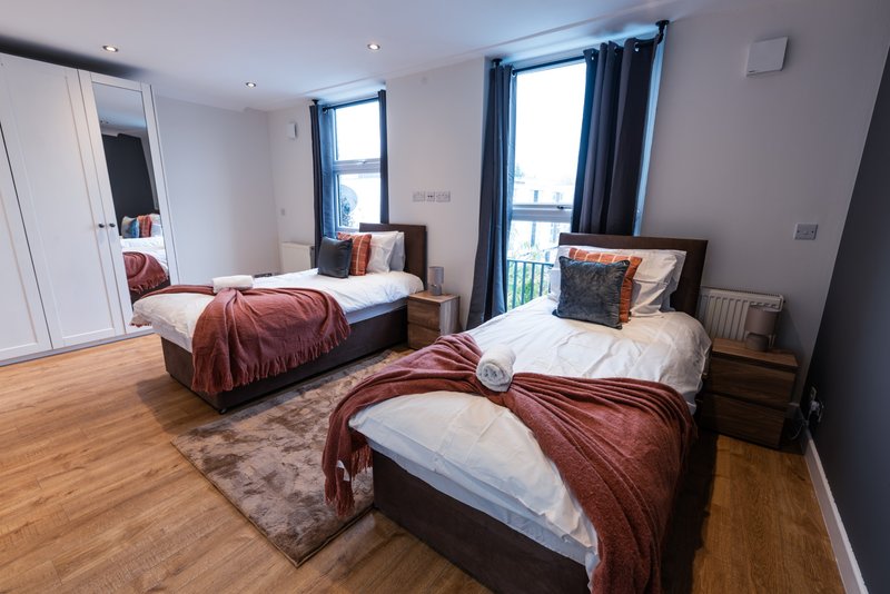 Bright bedroom with three single beds, burgundy bedding, wooden floor and blue curtains