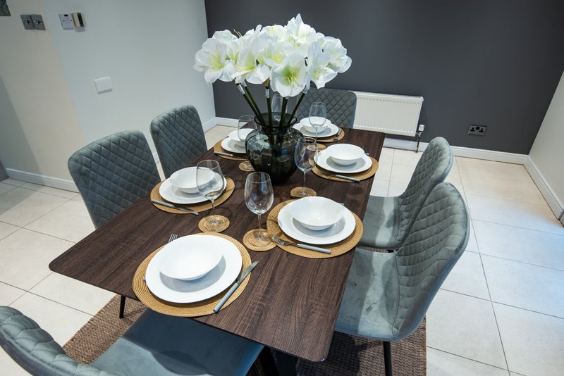 Dining table set for six with white flowers, place settings, and gray upholstered chairs