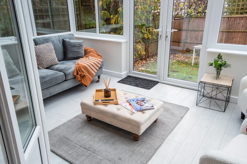 Bright modern sunroom with gray sofa, cream ottoman, magazines on table, garden views